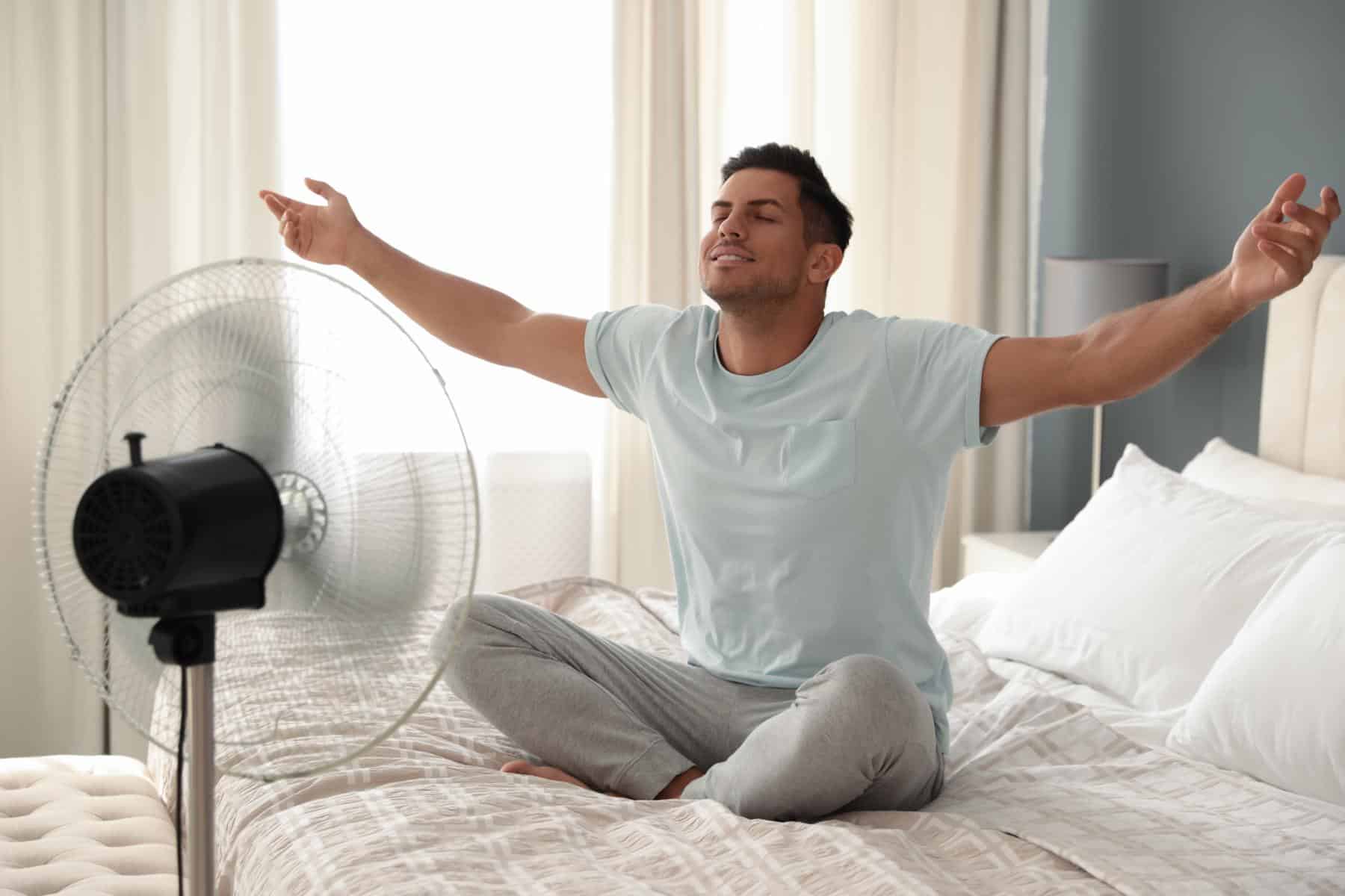 Mann kühlt sich mit Ventilator im Bett